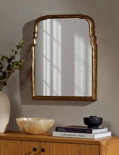 a wooden dresser topped with a mirror next to a vase filled with flowers and books