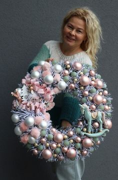 a woman is holding a wreath with ornaments on it