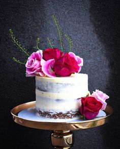 a white cake with pink and red flowers on top is sitting on a gold plate