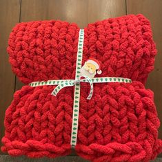 two red knitted blankets wrapped in green and white ribbon with a teddy bear on top