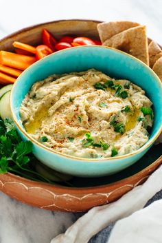 a bowl filled with hummus, carrots and crackers