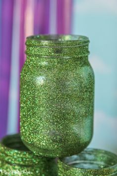 green glitter jars stacked on top of each other in front of purple and blue background