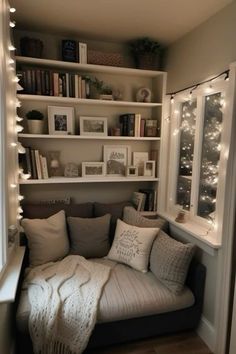 a couch with pillows and blankets in front of bookshelves filled with christmas lights