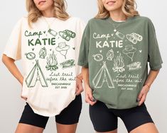 two women standing next to each other in shorts and t - shirts with camping related designs on them