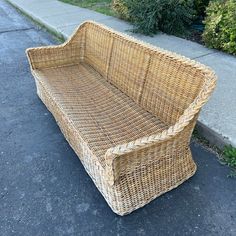 a wicker couch sitting on the side of a road next to a sidewalk and bushes