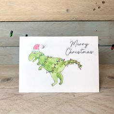 a christmas card with a green dinosaur wearing a santa's hat and lights on it