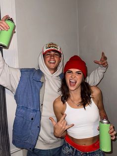 two people dressed in costumes holding cans and posing for the camera with their hands up