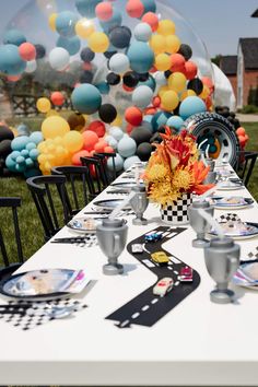 a long table with plates and place settings on it in front of an assortment of balloons