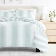 a bed with blue and white striped comforter in a clean bedroom area next to a dresser