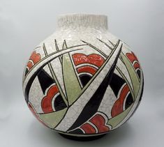 a white vase with black, red and green designs on the bottom is shown in front of a gray background