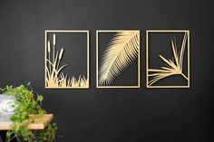 three metal wall art pieces hanging on a black wall next to a potted plant