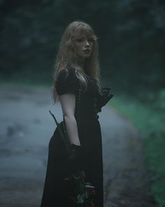 a woman with long blonde hair and black dress standing on a road in the dark