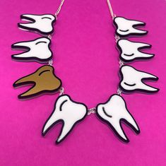 Tooth 🦷 fairy necklace is a fun, quirky accessory to pair with a any outfit. The necklace is made from white, gold and black gloss acrylic layered on a clear background. The teeth are linked together using jump rings and is linked to a curb chain with a lobster claw clasp.  Just leave a note 📝 at checkout with the word or name you would like made. If you have any questions drop us a line!💌 We are more than happy to help😁 To clean your necklace you can simply wipe with a glasses cloth or soft cloth to remove finger marks. Acrylic is a fragile material so please store in a jewellery box to prevent damage.  As ever for safety please keep away from small children. Novelty White Handmade Necklace, Handmade White Novelty Necklace, Plastic Jewellery, Laser Cut Jewelry, Fairy Necklace, Black Gloss, Clear Background, Statement Jewellery, Plastic Jewelry