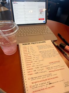 an open notebook sitting on top of a wooden table next to a cup of coffee