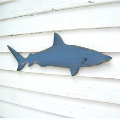 a blue metal shark on the side of a white house with wood slats behind it