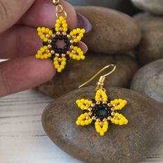 a pair of yellow and black beaded earrings sitting on top of rocks next to stones