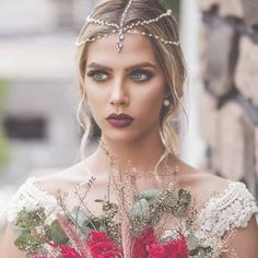 a woman in a wedding dress holding a bouquet with red and white flowers on it