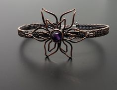 a silver bracelet with a purple stone in the center on a black surface, close up