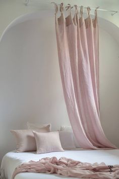 a white bed with pink sheets and pillows on it's headboard, hanging from the ceiling