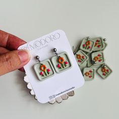 a pair of earrings with flowers on them are being held up by a person's hand