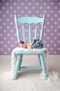 a baby laying on top of a blue chair in front of a polka dot wall