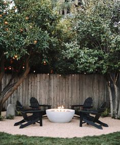 an outdoor fire pit surrounded by lawn chairs and trees with oranges in the background