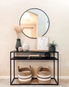 a black console table with two baskets and a round mirror on the wall above it