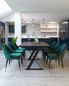 a dining room table with green chairs and blue cabinets in the back ground, next to an open kitchen area