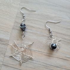 two spider web earrings with black beads and silver wire hanging from them on a wooden surface