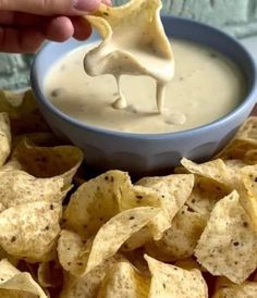 a person dipping tortilla chips into a blue bowl filled with white ranch dip