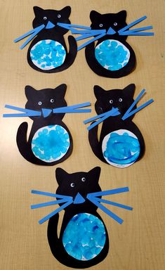 four black cats made out of paper on a wooden table with blue tape around them