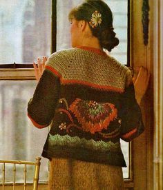 a woman standing in front of a window looking out at the street and wearing a sweater