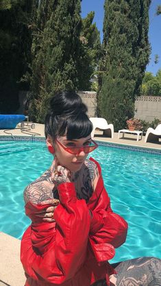 a woman sitting in front of a swimming pool with tattoos on her arm and leg