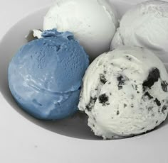 three ice creams in a white bowl with one blue and one chocolate chip cookie