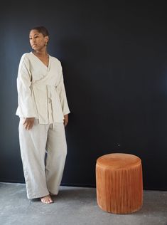 a woman standing in front of a black wall next to an orange stool and ottoman