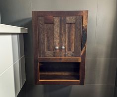 a small wooden cabinet in the corner of a bathroom wall mounted above a toilet paper dispenser