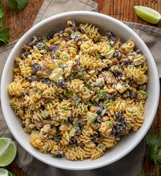 a white bowl filled with pasta salad next to limes