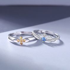 two rings with different designs on them sitting on top of a white surface and one has a gold fleur de li