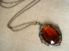 a necklace with an orange stone in the center on a white cloth covered tablecloth