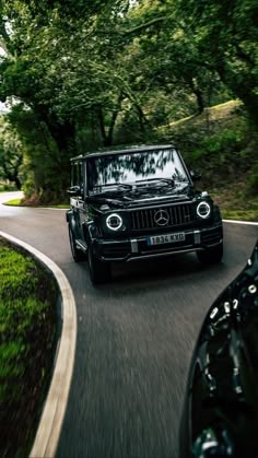 a black mercedes g class driving down a road in front of another car on the other side