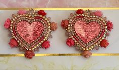 two pink heart shaped earrings with flowers and beads hanging from the side of a wall