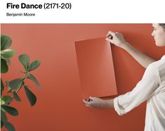 a woman is holding up a piece of paper on a red wall next to a potted plant