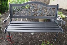 a black bench sitting in the middle of a yard next to a tree and shrubbery