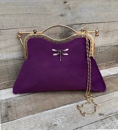 Stunning, handmade, purple velvet clutch bag with dragonfly detail. The lining is made with a beautiful fabric. Use it as a classic clutch or attach the shoulder strap to wear over your shoulder or as a crossbody. - Gold colour Chain strap (detachable) - Gold colour Kiss clasp (20.5cm) - Rhinestone dragonfly (not detachable) - H:21.5cm (handle not included) x W:29.5cm x D:5cm approximately The pattern of the lining inside of the bag may vary. But don't worry, I always make sure the lining of the Purple Pouch Clutch As Gift, Purple Handmade Wedding Bags, Elegant Purple Clutch For Everyday Use, Elegant Purple Handheld Bag, Elegant Purple Bag Gift, Purple Shoulder Bag With Detachable Handle As Gift, Handmade Purple Clutch Shoulder Bag, Purple Handheld Clutch For Everyday Use, Elegant Purple Clutch Bag