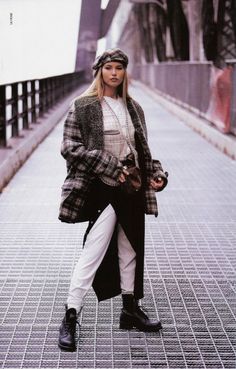 a woman is walking down the street wearing a plaid coat and white pants with black boots