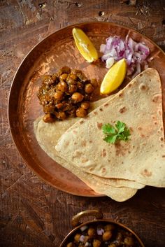 two pita breads on a plate with some garbanzo beans and lemon wedges