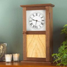 a wooden clock sitting on top of a table next to a potted green plant