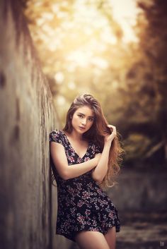 a woman leaning against a wall with her hair blowing in the wind and looking at the camera