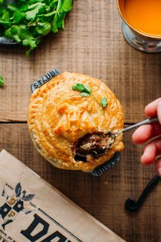 a hand holding a pastry over a wooden table next to a cup of green tea