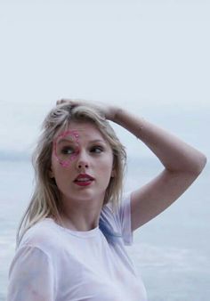 a woman with her hand on her head near the ocean and looking at the camera